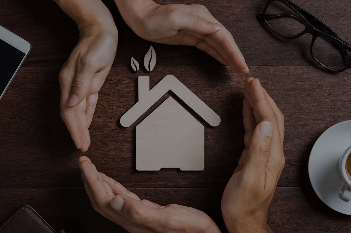 Hands surrounding a wooden home figurine — symbolic of protecting what matters